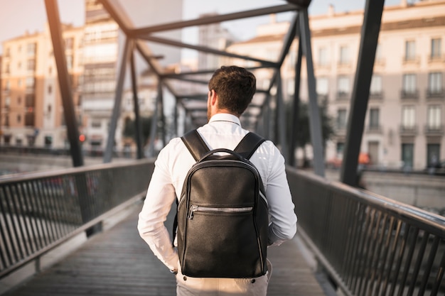 Rear view of a man with black backpack standing on bridge Premium Photo