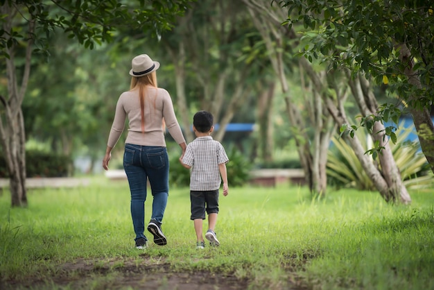 Rear view of mother and son walking together in home garden holding ...