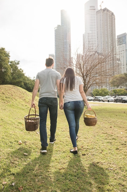 都市公園で歩くピクニックバスケットを持つカップルの後ろ姿 無料の写真