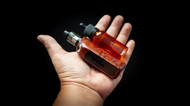 Rebuildable tank atomizer with high end stabilized redwood burl regulated box mods and e-liquid bottle in hand Premium Photo
