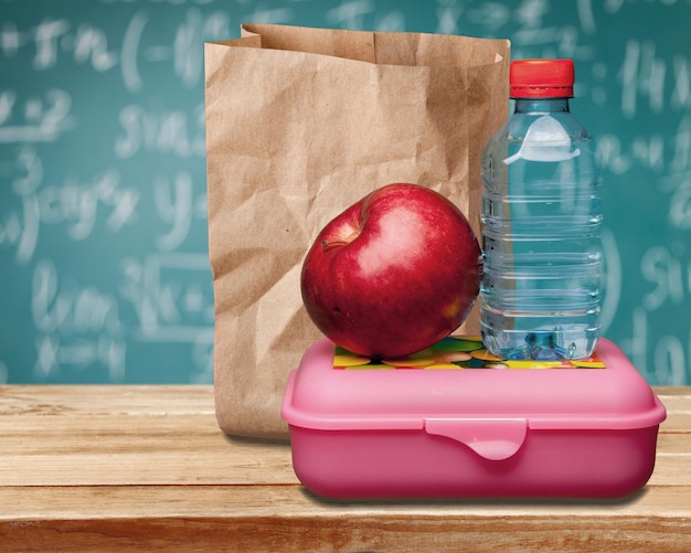 Premium Photo | Red apple with water and food on the school desk