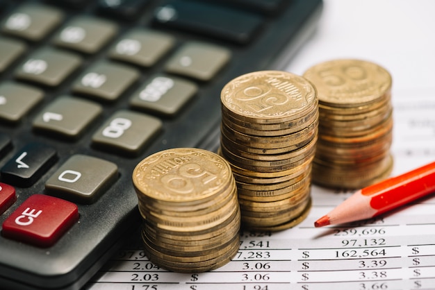 Red colored pencil with calculator and stack of coins over the financial report Free Photo