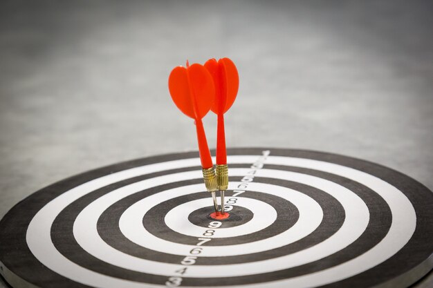Red dart arrow hitting in the target center of dartboard on bullseye with sun light vintage style Premium Photo