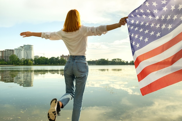 Red haired girl holding usa national flag in her hands. positive young woman celebrating united stat