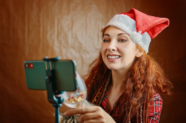 Premium Photo Red Haired Woman With Santa Hat And Dreadlocks Clinks Glass On Smartphone Virtual Talking With Parents And Using Video Chat Christmas Video Call