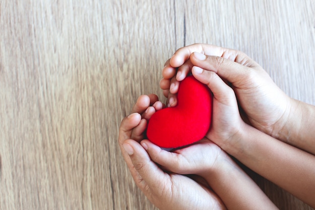 Premium Photo | Red heart in child hands and parent hands on wooden ...