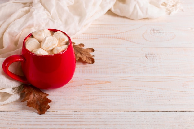 スカーフと乾燥した葉の背景に ココアとマシュマロの赤いマグカップ 秋の気分 温かい飲み物 プレミアム写真
