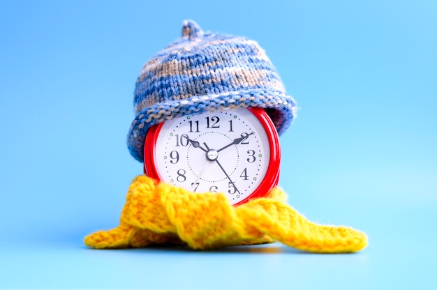 Premium Photo Red Round Alarm Clock In Knitted Wool Blue Hat And Yellow Scarf