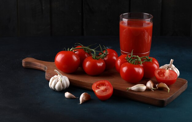 無料の写真 赤いトマトと青の背景にジュースのグラスと木の板にニンニクの手袋