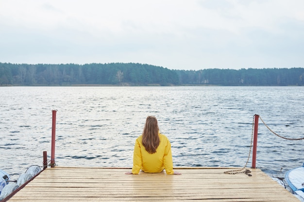 Premium Photo | Redhead woman in yellow raincoat sitting on the pier of ...