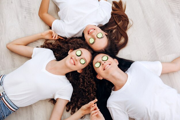 Refreshing eye mask. beautiful smiling girls and their mother lie on the floor, make a face mask of 