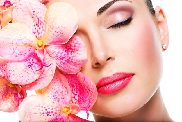 Relaxed beautiful face of a young girl with clear skin and pink orchids. beauty treatment concept Free Photo