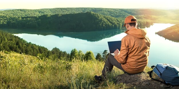  Remote freelancer work in nature.  beautiful view with sunset and lake in background. banner.