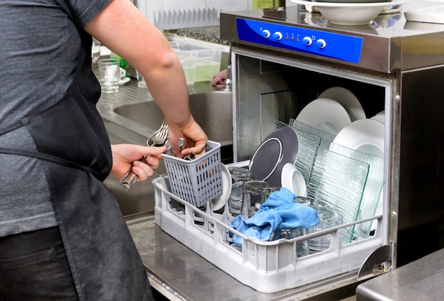 Restaurant kitchen worker emptying a dishwasher removing clean cutlery from the basket in a close up on his hands Premium Photo