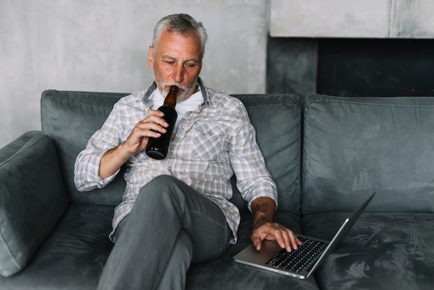 Retired man drinking beer from bottle using laptop Free Photo