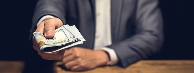 Rich businessman holding and  giving us dollar money in dark private room Premium Photo