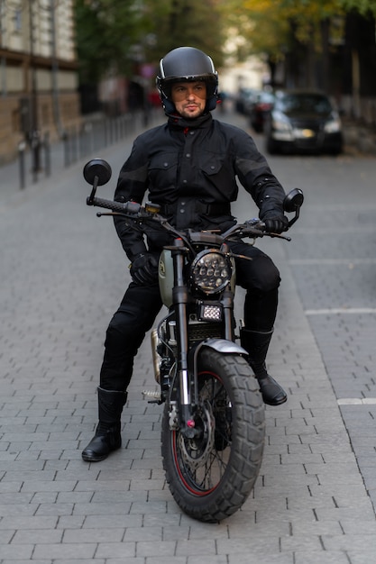 ひげと口ひげを持つ黒のファッションサングラスと正しいバイカージャケットのライダー男は 日没でクラシックなスタイルのレーサーバイクに座っています 残忍な楽しい都会のライフスタイル プレミアム写真