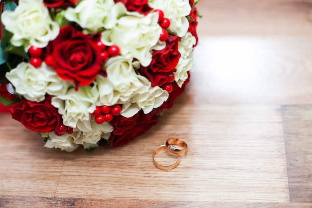 Premium Photo | Rings and a wedding bouquet of red and white roses on table