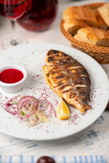 Roasted grilled fish served with herbs, lemon, onion salad and dip red tomato sauce. Free Photo