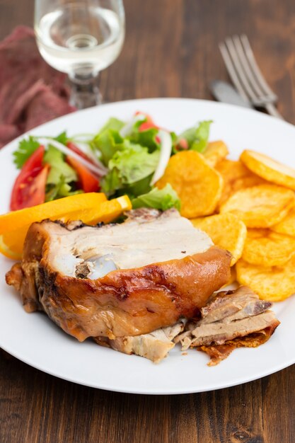 Premium Photo | Roasted piglet with potato chips and orange on white plate