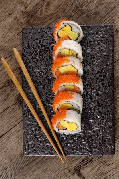 Roll sushi with chopsticks on a black plate | Free Photo