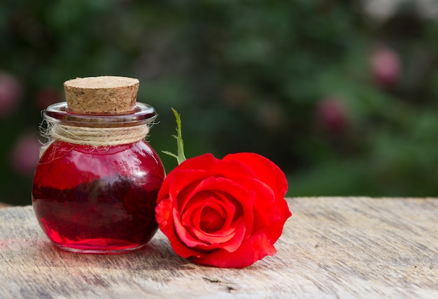 Rose essential oil in a round bottle and red rose | Premium Photo