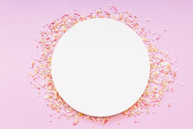 Round blank white frame surrounded with sprinkles on pink background Free Photo