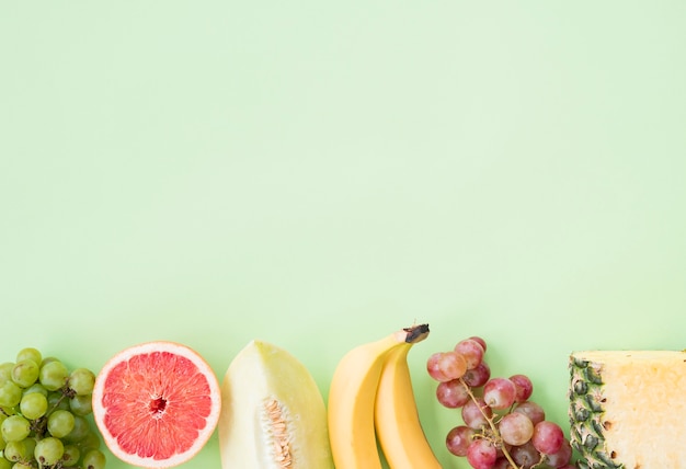 Row of grapes; grapefruit; muskmelon; banana; grapes and pineapple on pastel background Free Photo