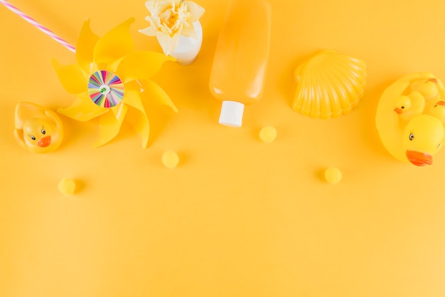 ゴム製のアヒル 風車 日焼け止めローションボトル 黄色の背景に小さなポンポンとホタテ 無料の写真