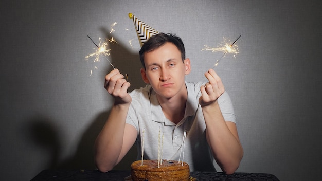 一人で誕生日を祝って 線香花火を保持しているパーティーハットの悲しい孤独な男 プレミアム写真