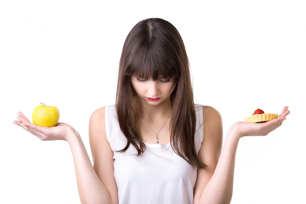 Sad woman with an apple in one hand and cake in the other Free Photo