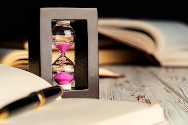 Premium Photo | Sandglass on wooden table with opened book close up