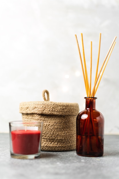 Scandinavian hygge style, home interior scent aroma diffuser with wooden sticks, small straw basket, red candle, Premium Photo