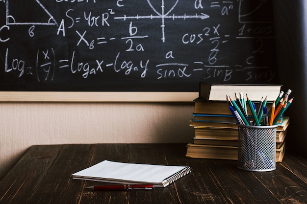 School desk in classroom, with books on background of chalk board with written formulas Premium Photo