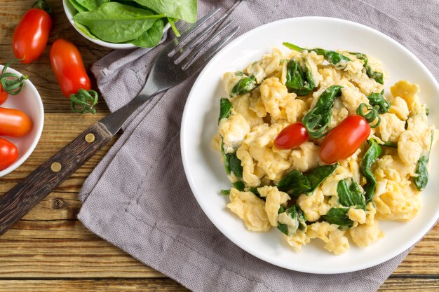 Premium Photo Scrambled Eggs With Spinach And Tomatoes On A White Plate On A Wooden Table