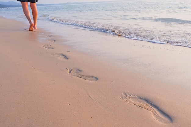 海での休暇 ビーチの上を歩く人 ビーチ旅行 砂に足跡を残して砂浜の上を歩く男 男性の足と黄金の砂のクローズアップの詳細 セレクティブフォーカス 素足の足をトレイル プレミアム写真
