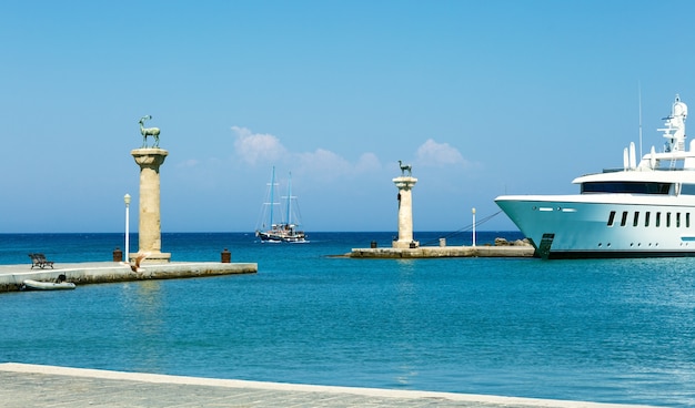 ギリシャのロードス島の巨像が立っていたマンドラキ港の入り口にある鹿の像と船の海の景色 プレミアム写真