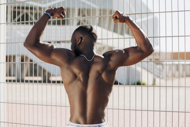 フェンスの前に裸の胸を持つ筋肉を持つ魅力的なアフリカ系アメリカ人男性 無料の写真