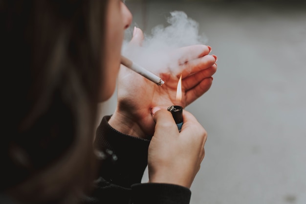 Selective closeup shot of a female lighting up a cigarette with a lighter Free Photo