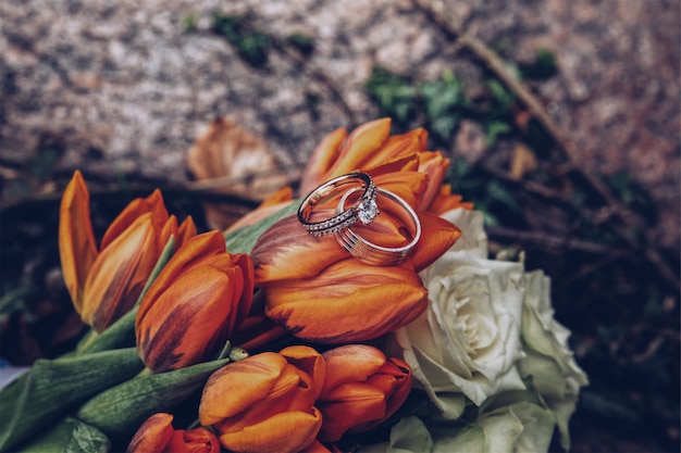 Selective closeup shot of silver diamond rings on orange tulips and white roses Free Photo