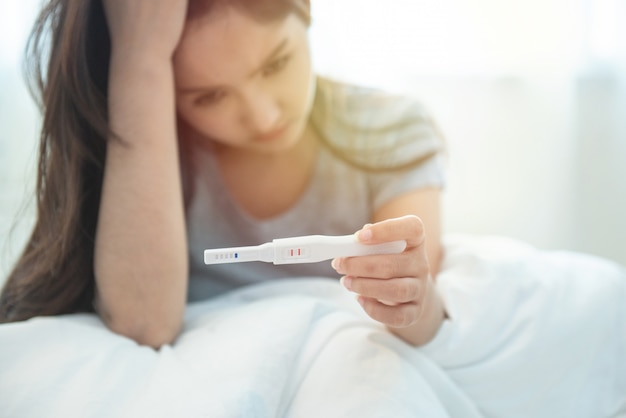 Selective focus on tester.unwanted maternity pregnant asian girl with pregnancy test in hand.asian lady concerned and unhappy with fertility test . Premium Photo