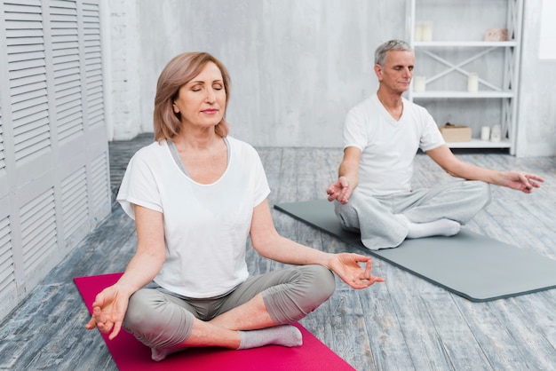 Senior couple performing meditation on exercise mat at home Free Photo