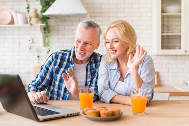 Senior couple waving their hands during online video call on laptop Free Photo