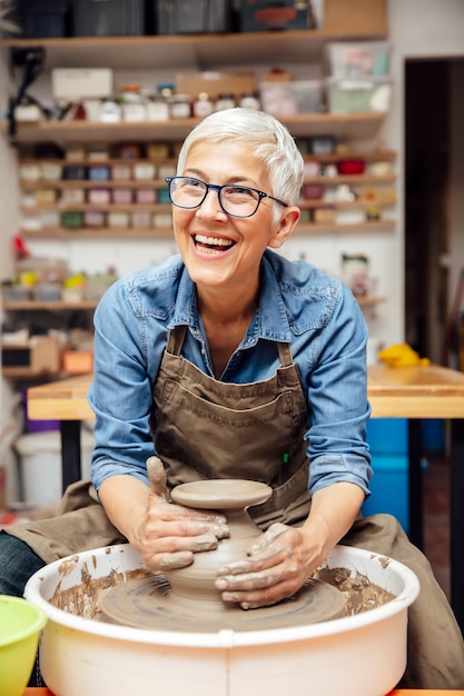 Premium Photo | Senior female potter working on pottery wheel while ...