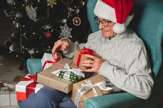 クリスマスプレゼントがたくさんあるサンタクロースの帽子をかぶった先輩が座っています プレミアム写真