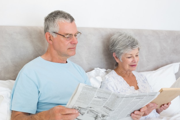 Premium Photo | Senior man holding newspaper with wife reading book in ...