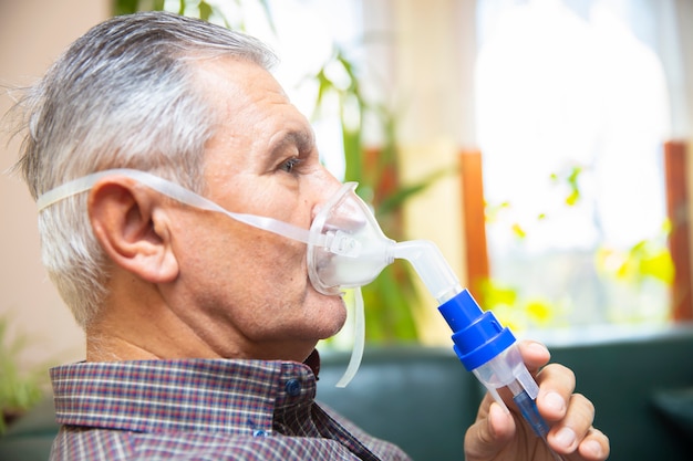 Premium Photo | Senior man using medical equipment for inhalation with ...