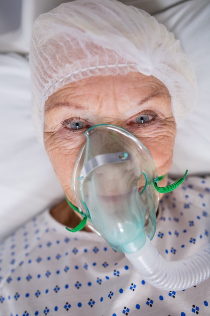 病院のベッドに横になっている酸素マスクを身に着けているシニアの患者 無料の写真