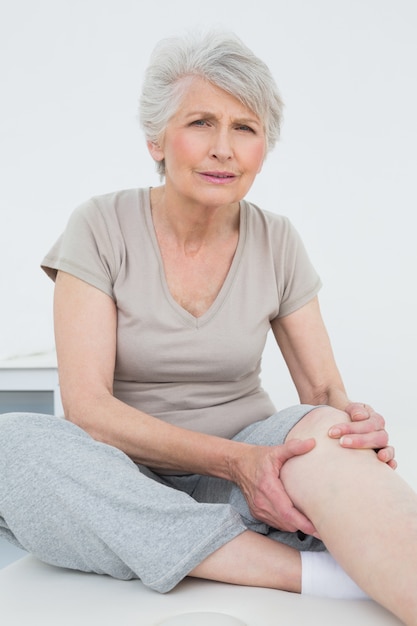 Senior woman with painful knee sitting on examination table Premium Photo