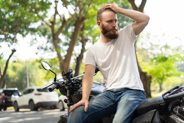 Serious biker leaning on broken motorbike Free Photo